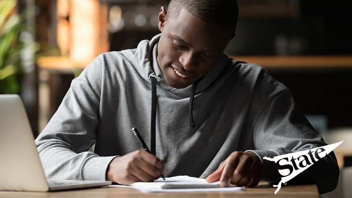 Student writes in a notebook in front of an open laptop computer. 