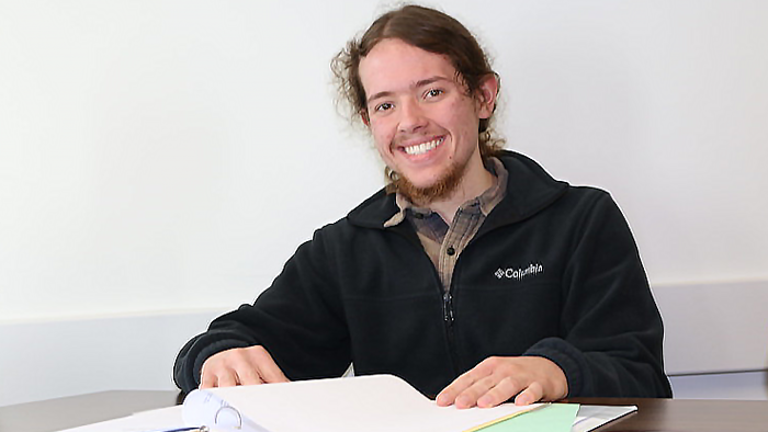 A student sitting at a table with a binder open, smiling at the camera