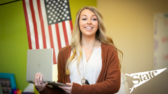 Woman standing with a laptop in hand, smiling at the class