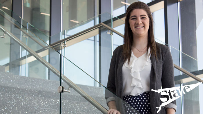 A smiling female who graduated with a finance degree standing on the stairwell in Strong Hall.